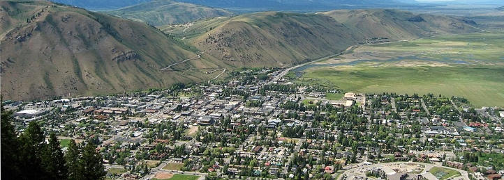 Mountain valley town surrounded by rolling hills, green fields, and winding roads.