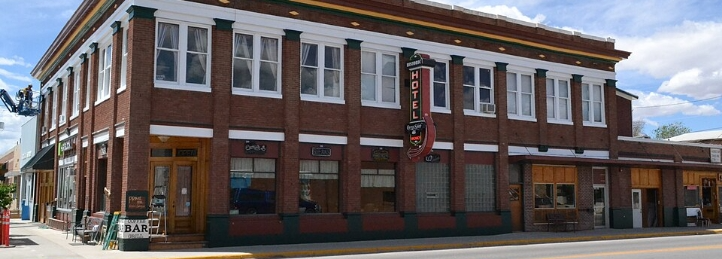 Historic two-story brick hotel with large windows, street-level businesses, and a vertical hotel sign.