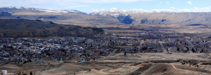 Panoramic view of a small town in a rugged valley surrounded by rolling hills and snow-capped mountains.
